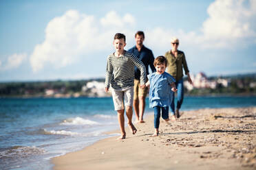 Young family with two small children walking barefoot outdoors on beach. - HPIF20627