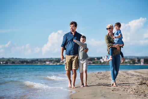 Junge Familie mit zwei kleinen Kindern läuft barfuß am Strand. - HPIF20629