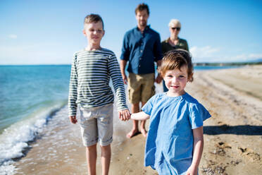 Junge Familie mit zwei kleinen Kindern, die am Strand spazieren gehen und sich an den Händen halten. - HPIF20630