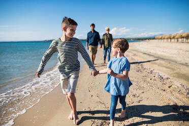 Junge Familie mit zwei kleinen Kindern, die barfuß am Strand laufen und Spaß haben. - HPIF20631