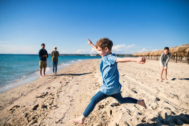 Ein fröhliches kleines Mädchen mit Familie läuft draußen am Sandstrand und hat Spaß. - HPIF20633