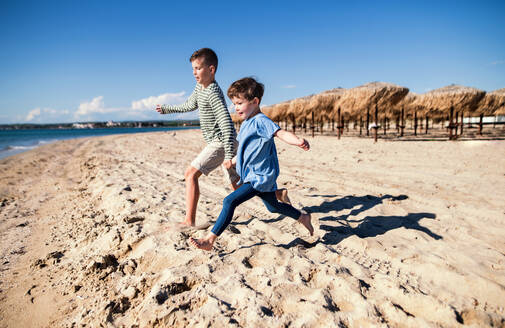 Zwei kleine Kinder laufen draußen am Sandstrand und halten sich an den Händen. - HPIF20634