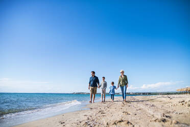 Junge Familie mit zwei kleinen Kindern läuft barfuß am Strand. - HPIF20637