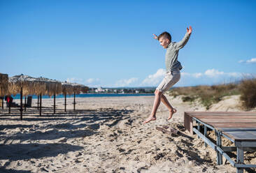 A cheerful small boy playing outdoors on sand beach, jumping. - HPIF20641