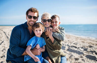 Portrait of young family with two small children sitting outdoors on beach. - HPIF20644