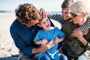 Porträt einer jungen Familie mit zwei kleinen Kindern, die draußen am Strand sitzen und Spaß haben. - HPIF20645