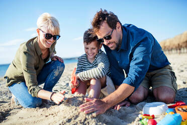 A young family with small boy sitting outdoors on beach, playing. - HPIF20647