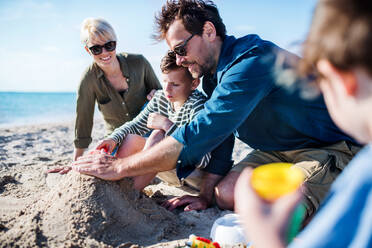 Junge Familie mit zwei kleinen Kindern, die im Freien am Strand sitzen und mit Sand spielen. - HPIF20648