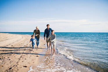 Junge Familie mit zwei kleinen Kindern, die draußen am Strand barfuß laufen. - HPIF20653