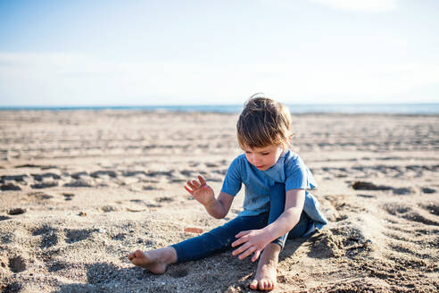 Ein glückliches kleines Mädchen, das draußen am Strand im Sand spielt. - HPIF20657