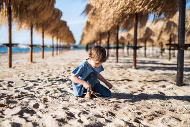 Ein kleines Mädchen spielt unter Strohsonnenschirmen im Freien am Sandstrand. - HPIF20660