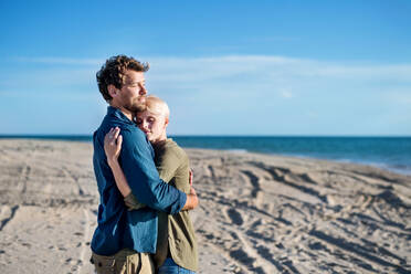 A young couple standing outdoors on beach, hugging. Copy space. - HPIF20665