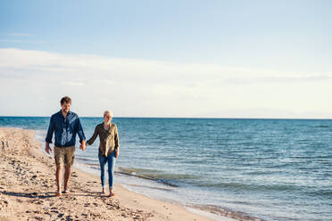 Ein junges Paar, das am Strand spazieren geht und sich an den Händen hält. Copy space. - HPIF20670