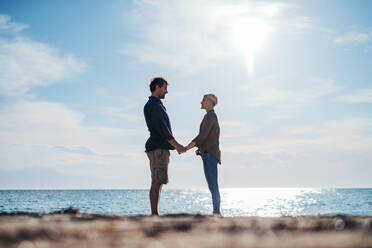 Ein junges Paar steht im Freien am Strand und hält sich an den Händen. Platz kopieren. - HPIF20672