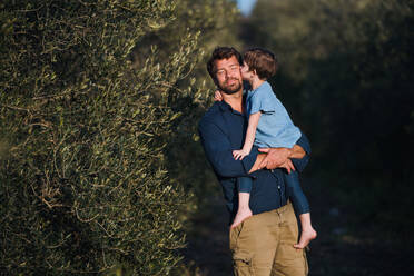 Glücklicher Vater mit kleiner Tochter steht im Freien unter einem Olivenbaum und küsst sich. - HPIF20685