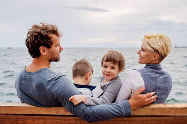 Junge Familie mit zwei kleinen Kindern sitzt auf einer Bank im Freien am Strand, Rückansicht. - HPIF20702