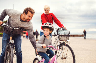 A young family and small daughter with bicycles outdoors on beach. - HPIF20704