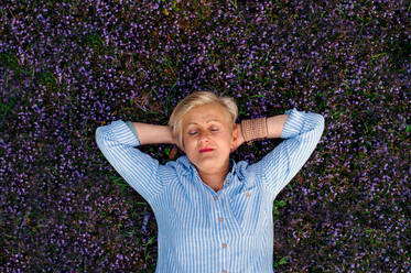 Draufsicht auf eine ältere Frau mit geschlossenen Augen, die auf Blumen im Gras auf einer Wiese liegt. - HPIF20717