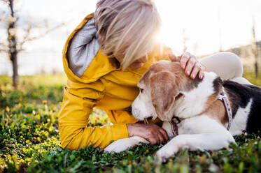 Vorderansicht einer älteren Frau, die im Frühling im Gras liegt und ihren Hund streichelt. - HPIF20730