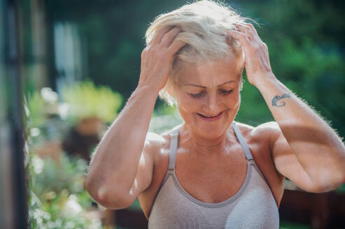 Vorderansicht einer älteren Frau mit Sport-BH, die im Sommer auf einer Terrasse steht. - HPIF20750