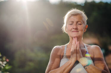 Eine ältere Frau mit Sport-BH steht im Sommer draußen auf einer Terrasse und macht Yoga. - HPIF20754