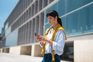 Mature businesswoman using smart phone in front of building - JOSEF19632