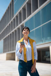 Thoughtful businesswoman with smart phone standing in front of building - JOSEF19637