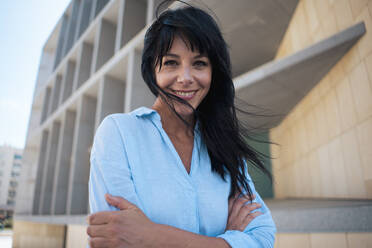 Smiling businesswoman with arms crossed in front of office building - JOSEF19691