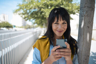 Smiling businesswoman with bangs holding mobile phone - JOSEF19705