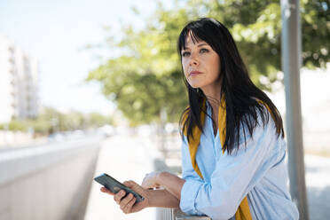 Contemplative businesswoman with long hair holding smart phone - JOSEF19711