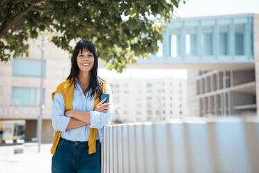 Smiling mature businesswoman with arms crossed leaning on railing - JOSEF19716