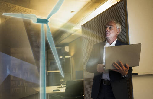 Digitales Kompositbild eines Geschäftsmannes mit Blick auf eine futuristische Windturbine im Büro - UUF28759