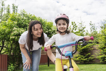 Smiling mother helping daughter riding bicycle in back yard - OSF01585