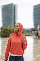 Smiling woman wearing hooded shirt traveling in city - JCCMF10398