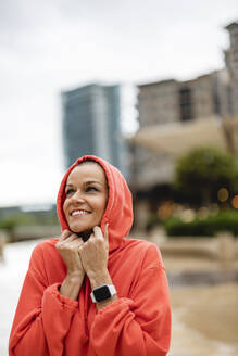 Smiling woman wearing hood in city - JCCMF10399