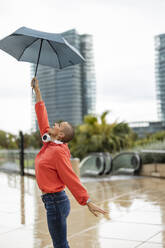 Playful shaved head woman holding umbrella in city - JCCMF10405