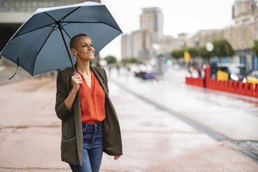 Smiling woman with umbrella standing on footpath - JCCMF10411