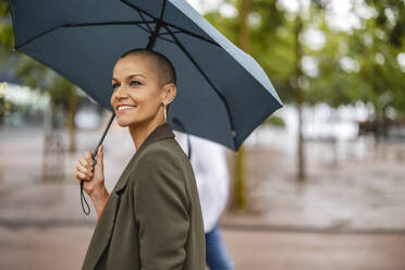 Smiling woman with shaved head holding umbrella - JCCMF10412