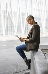 Woman using tablet PC sitting on by road in city - JCCMF10415