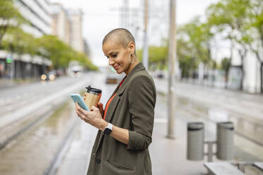 Woman using smart phone waiting at tram station platform - JCCMF10417