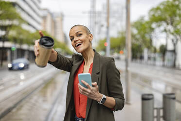 Woman with smart phone and drink container at tram station platform - JCCMF10418