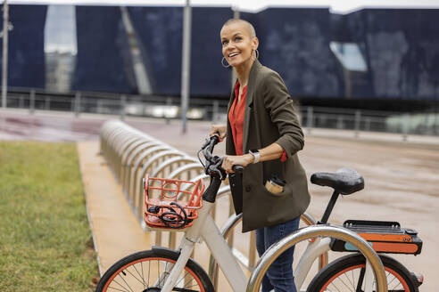 Woman holding bicycle at parking station - JCCMF10433