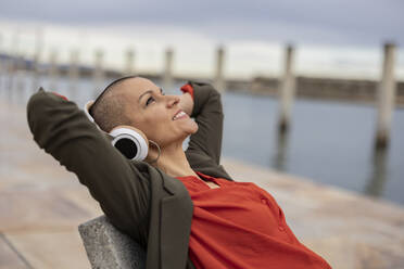Shaved head woman listening music with headphones relaxing at promenade - JCCMF10443