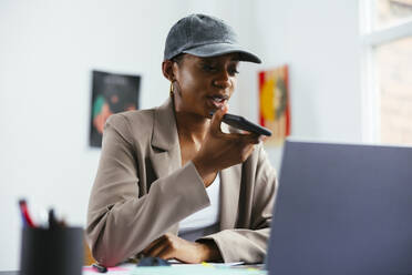 Young freelancer talking on speaker phone at office - EBSF03491