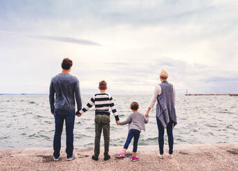 Rückansicht einer jungen Familie mit zwei kleinen Kindern, die händchenhaltend im Freien am Strand stehen. - HPIF20843