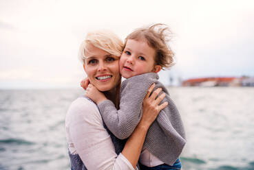Vorderansicht einer jungen Mutter mit ihrer kleinen Tochter, die im Freien am Strand steht. - HPIF20845
