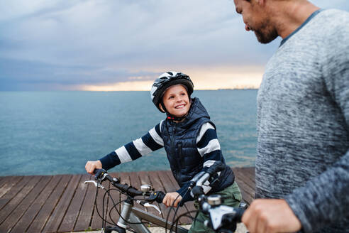 Unbekannter Vater und kleiner Sohn mit Fahrrädern im Freien am Strand stehend, im Gespräch. - HPIF20855