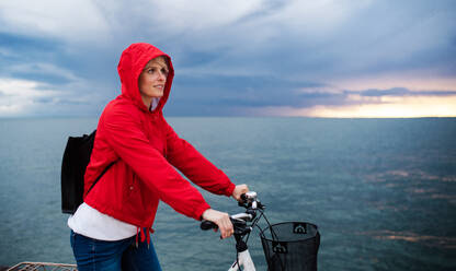 Side view of woman with bicycle standing outdoors on beach, resting. Copy space. - HPIF20856