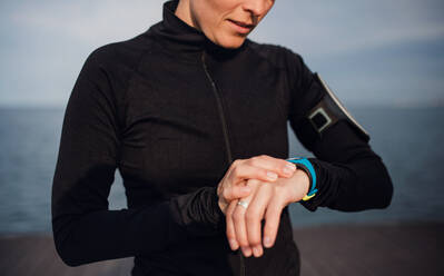 A midsection of young sportswoman standing outdoors on beach, using smartwatch. - HPIF20872