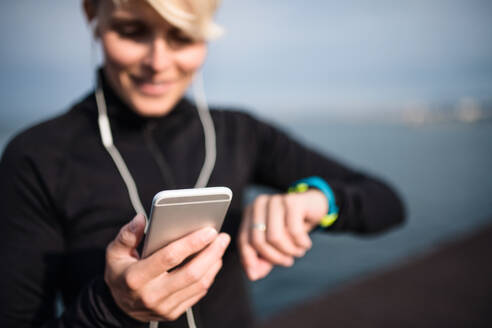 Eine junge Sportlerin mit Smartphone und Smartwatch steht im Freien am Strand. - HPIF20890